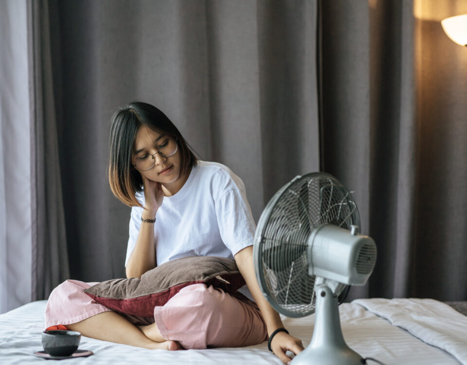 Pessoa a tentar dormir numa noite quente de verão, com expressão de desconforto, deitada numa cama com lençóis leves